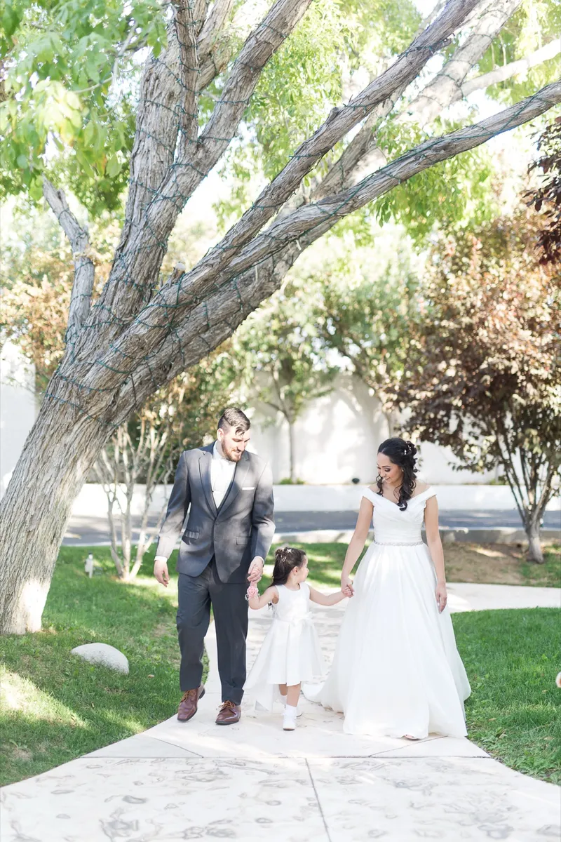 Couple walking a shaded garden path holding the hands of a little flower girl between them