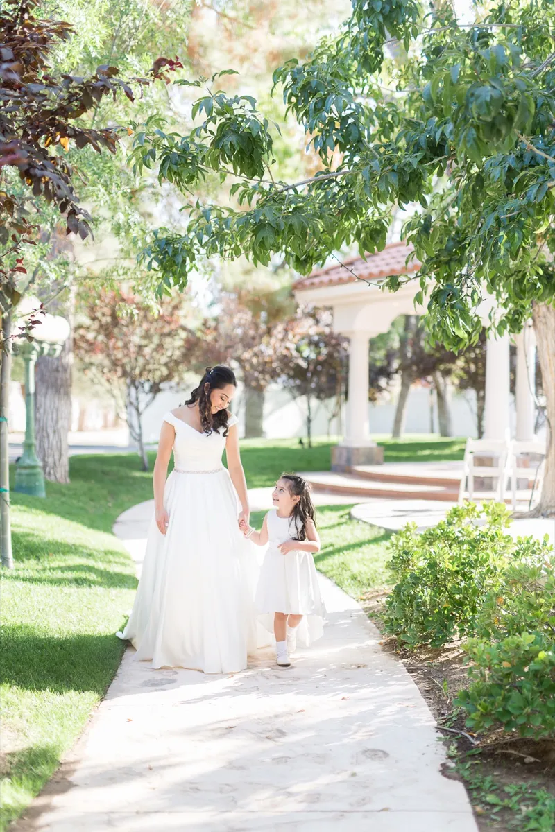 Bride walking the garden path hand in hand with a small flower girl in a white dress