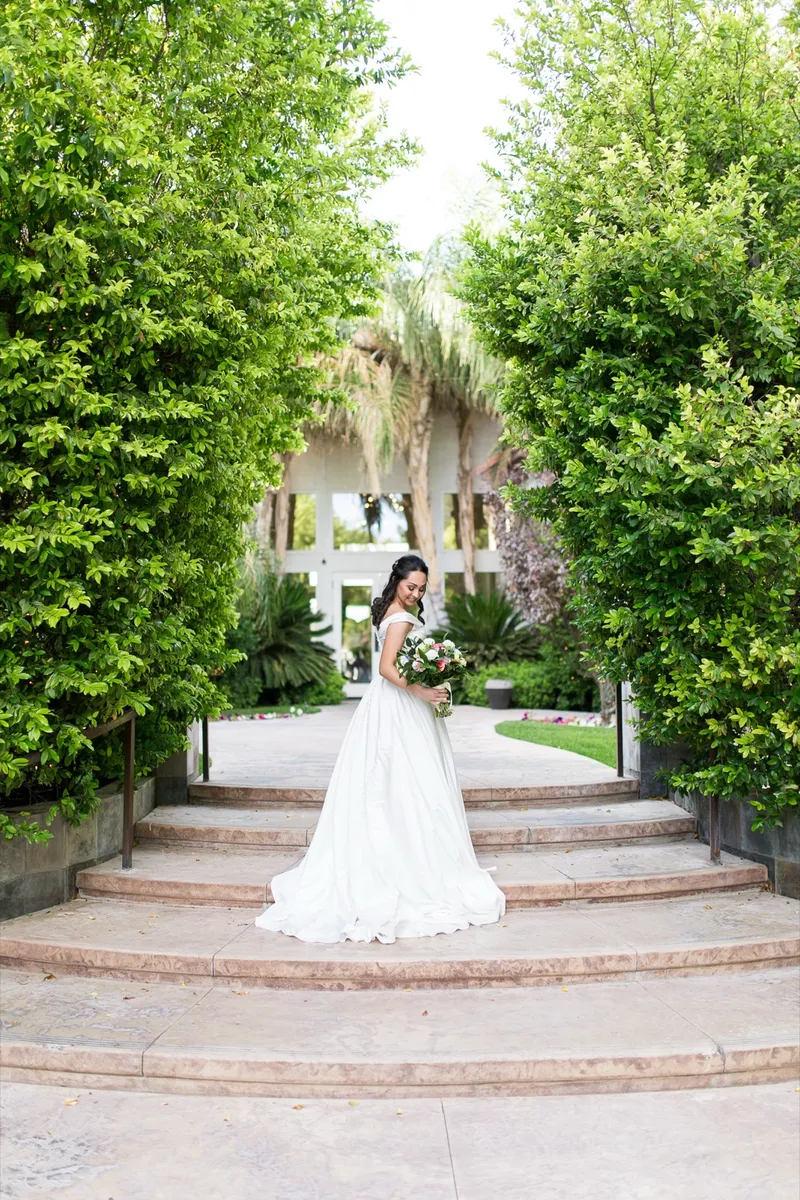 Bride standing at the top of a set of garden steps with tall hedges framing her on both sides