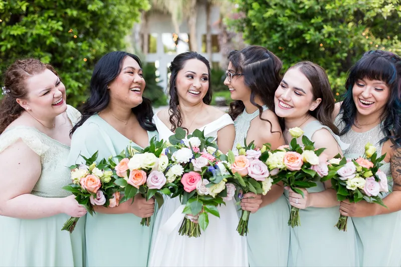 Bride laughing with her bridesmaids in mint dresses, all of them holding pastel bouquets