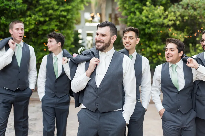 Groomsmen walking together in vests and shirtsleeves with their jackets slung over their shoulders