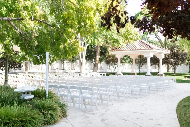 Rows of white folding chairs set on the garden patio facing the columned pavilion, nobody seated yet