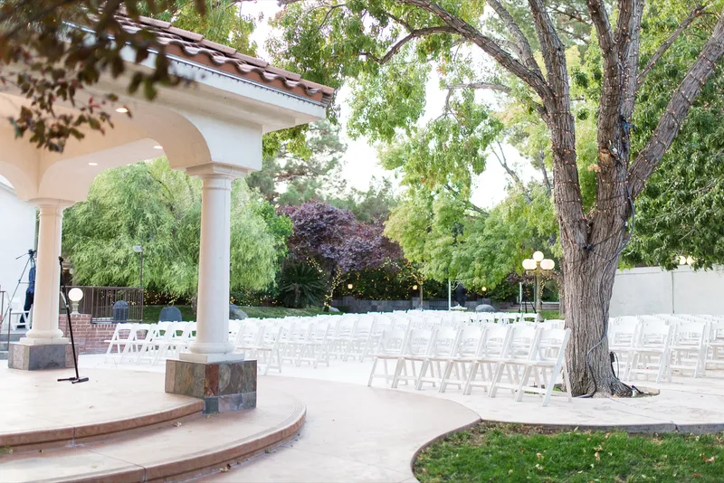 The empty ceremony site under the trees, a microphone stand in front of the pavilion and white chairs in two blocks