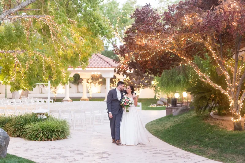 Couple standing together on the courtyard path at dusk with the trees above them full of small lights