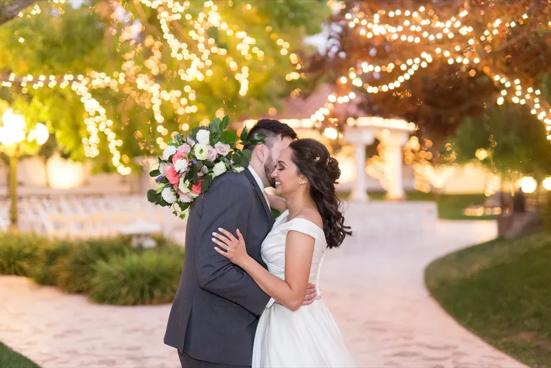 Couple holding each other on the courtyard with the string lights glowing warm through the branches behind