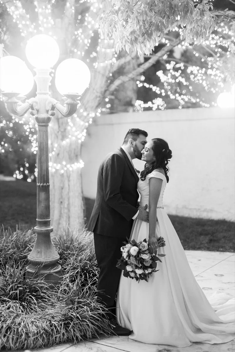 Black and white of the couple standing beside a globe lamppost with lit branches filling the background