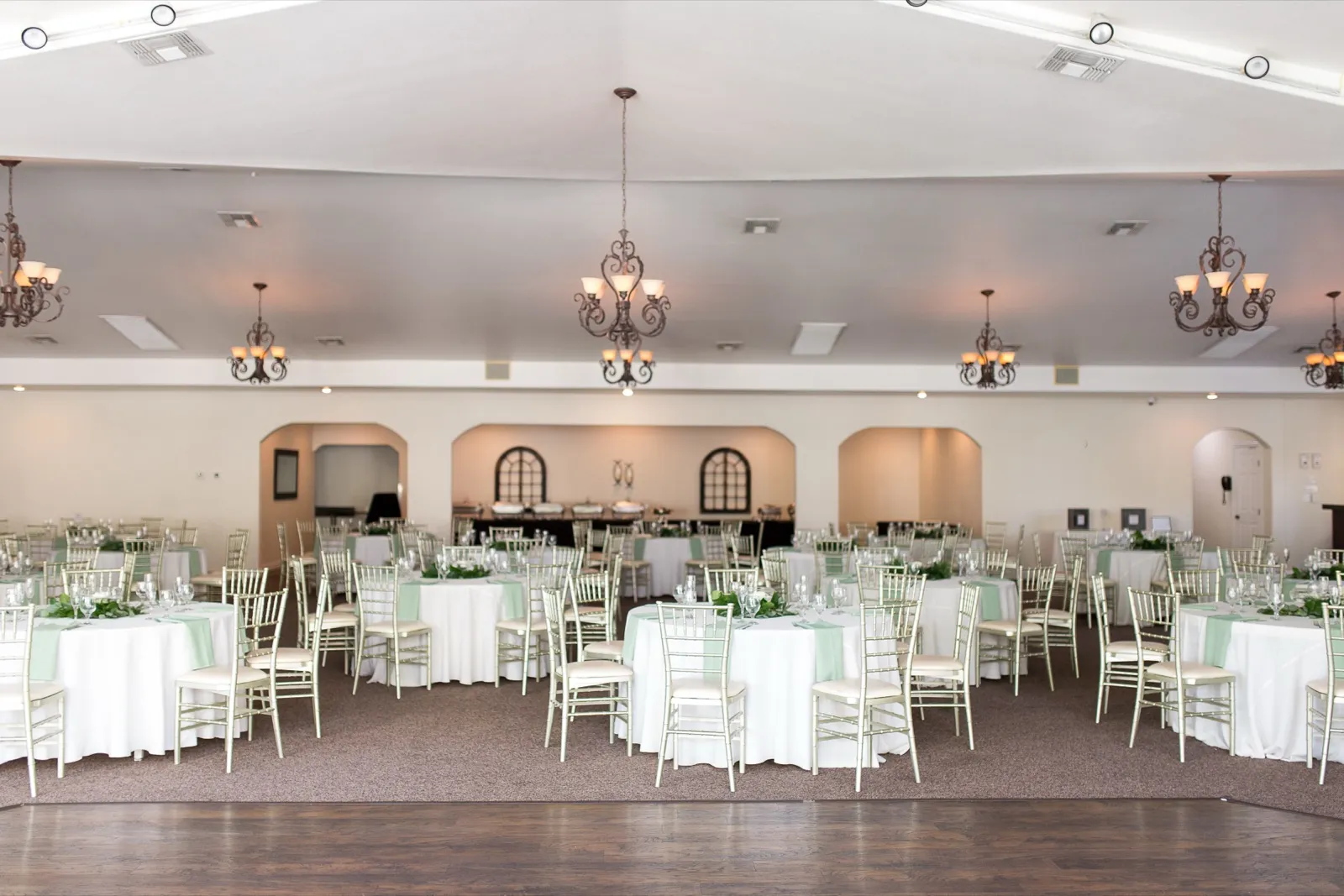 The banquet room set for a reception, round tables in white and mint under wrought iron chandeliers