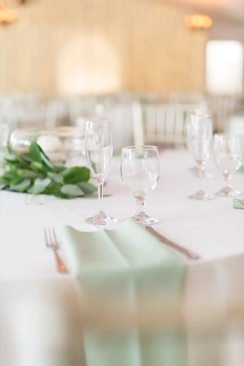 Close view of one place setting with a mint napkin folded over the plate and glassware catching the room light