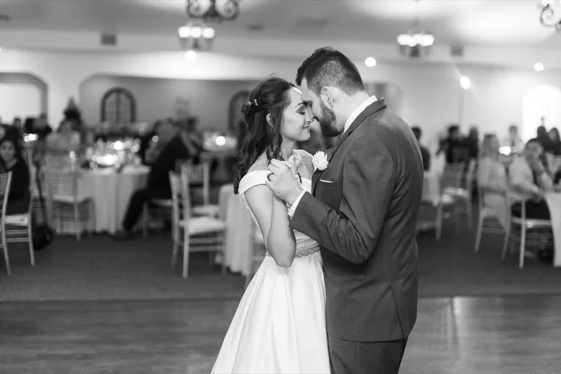 Black and white of the couple slow dancing on the wood floor while guests watch from the tables