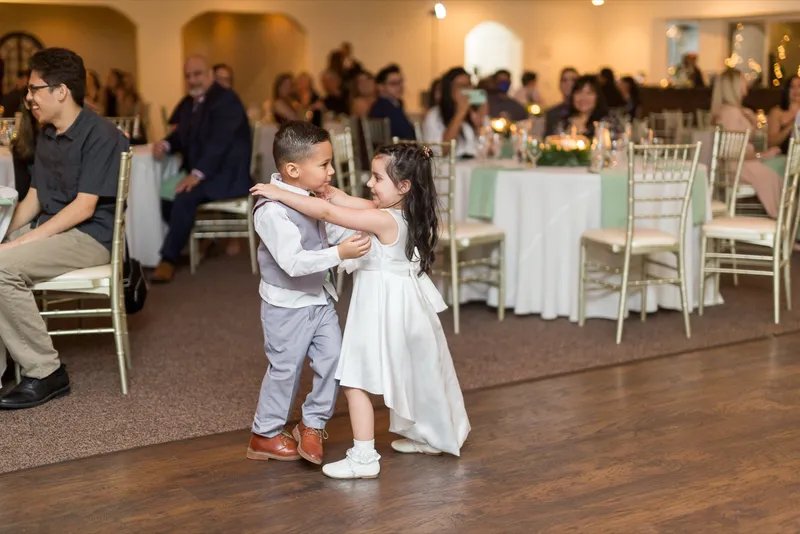 Two small children dancing together on the empty wood floor while guests eat behind them