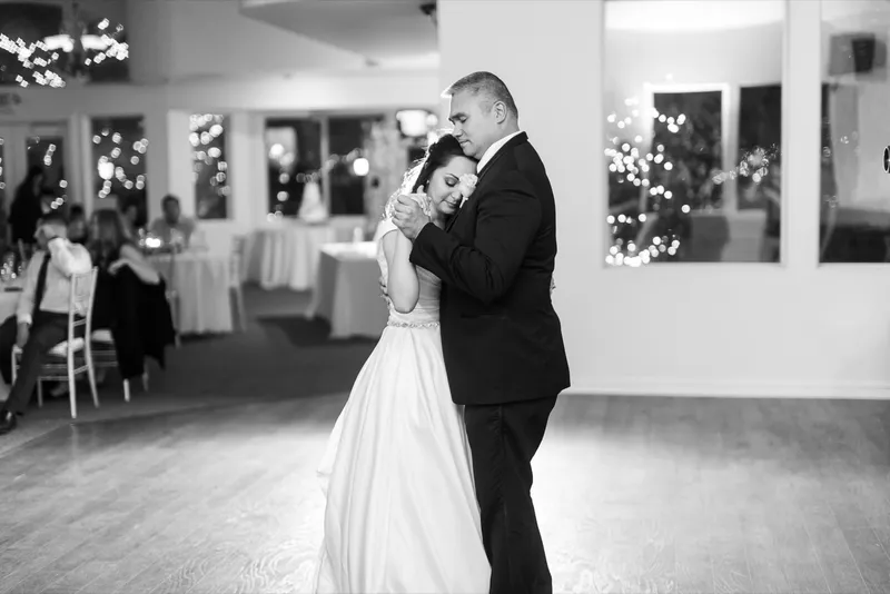 Black and white of the same parent dance with the lit trees visible through the window