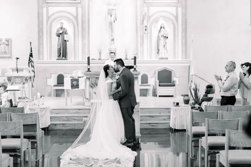 Black and white of the couple kissing at the front of the church with her long veil spread across the floor