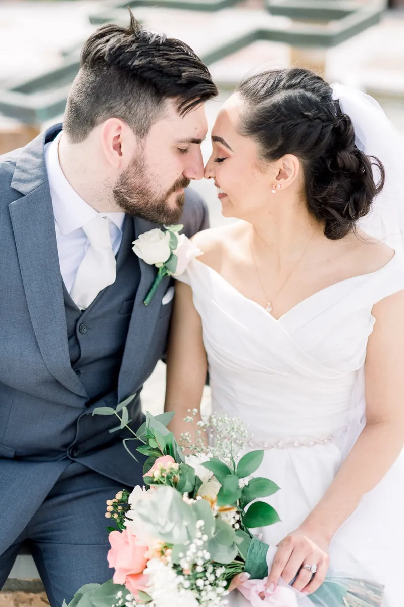 Close portrait of the couple with their noses touching and her peach and white bouquet in her lap