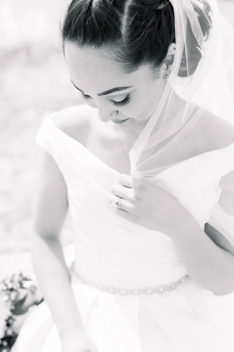 Black and white of the bride looking down at her gown with her veil over her shoulder