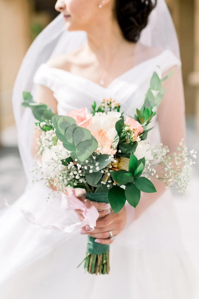 Close view of the peach and white bouquet held against the layers of her veil