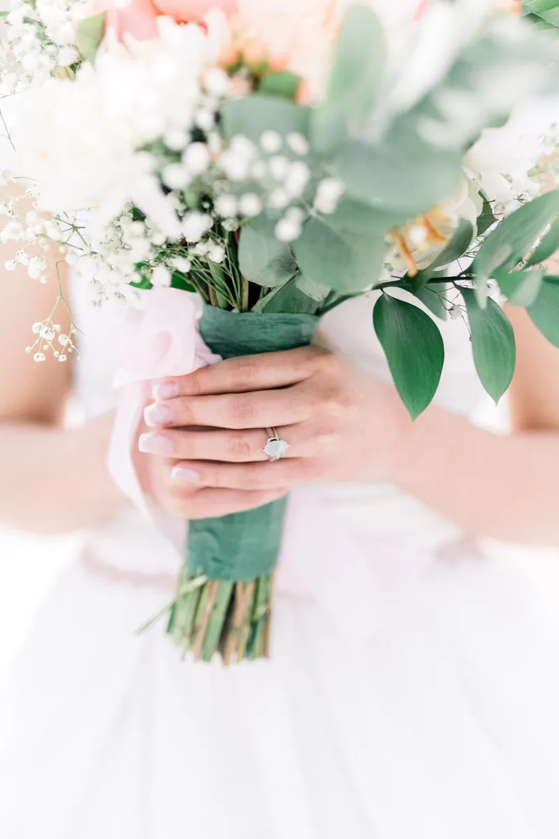 The bride's hand and her ring wrapped around the ribbon tied bouquet stems