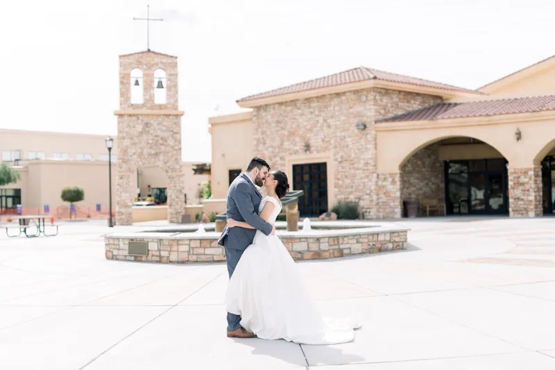 Couple kissing in the middle of the plaza with the bell tower and the arched church entry behind them