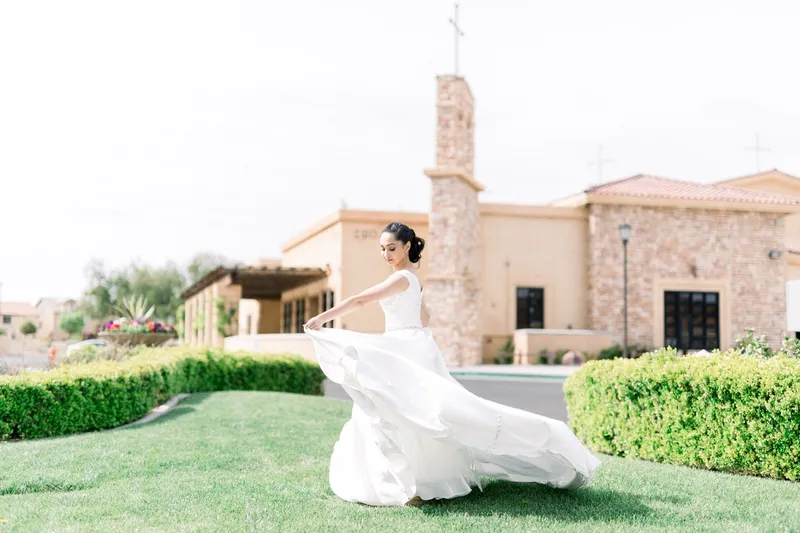 Bride sweeping the skirt of her gown across the lawn beside the church