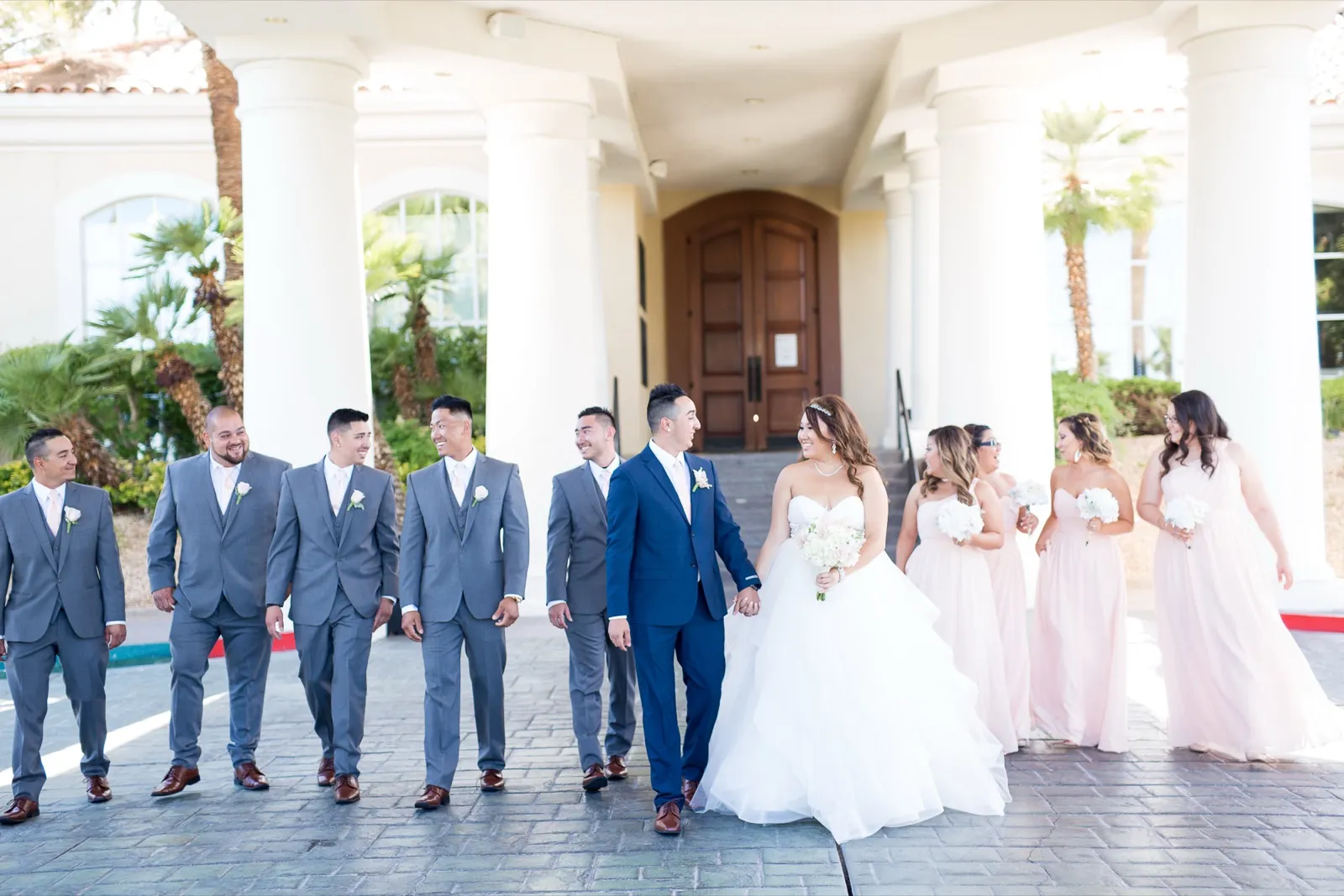 Wedding party walks under the clubhouse portico, groomsmen in grey suits and bridesmaids in blush