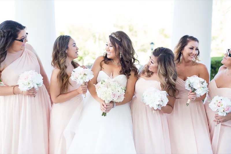 Bride laughing in a line with her bridesmaids, all of them holding white and blush bouquets