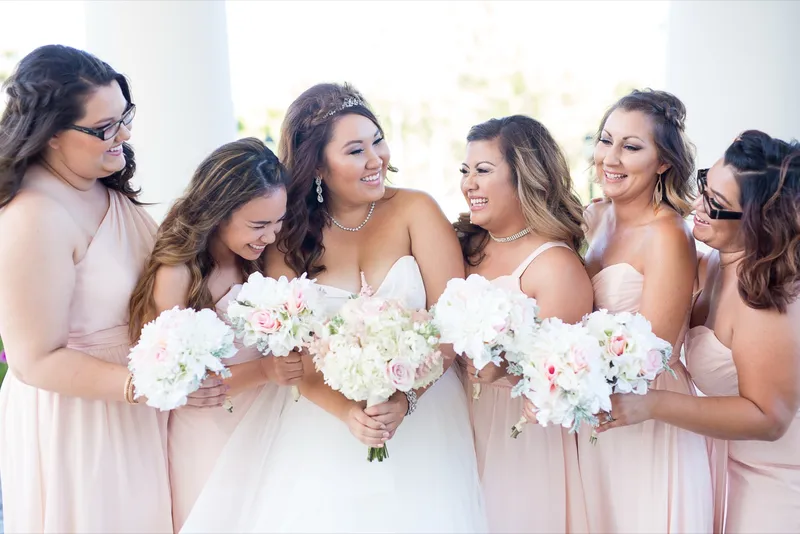 Bridesmaids leaning in around the bride with their bouquets held low, everyone laughing