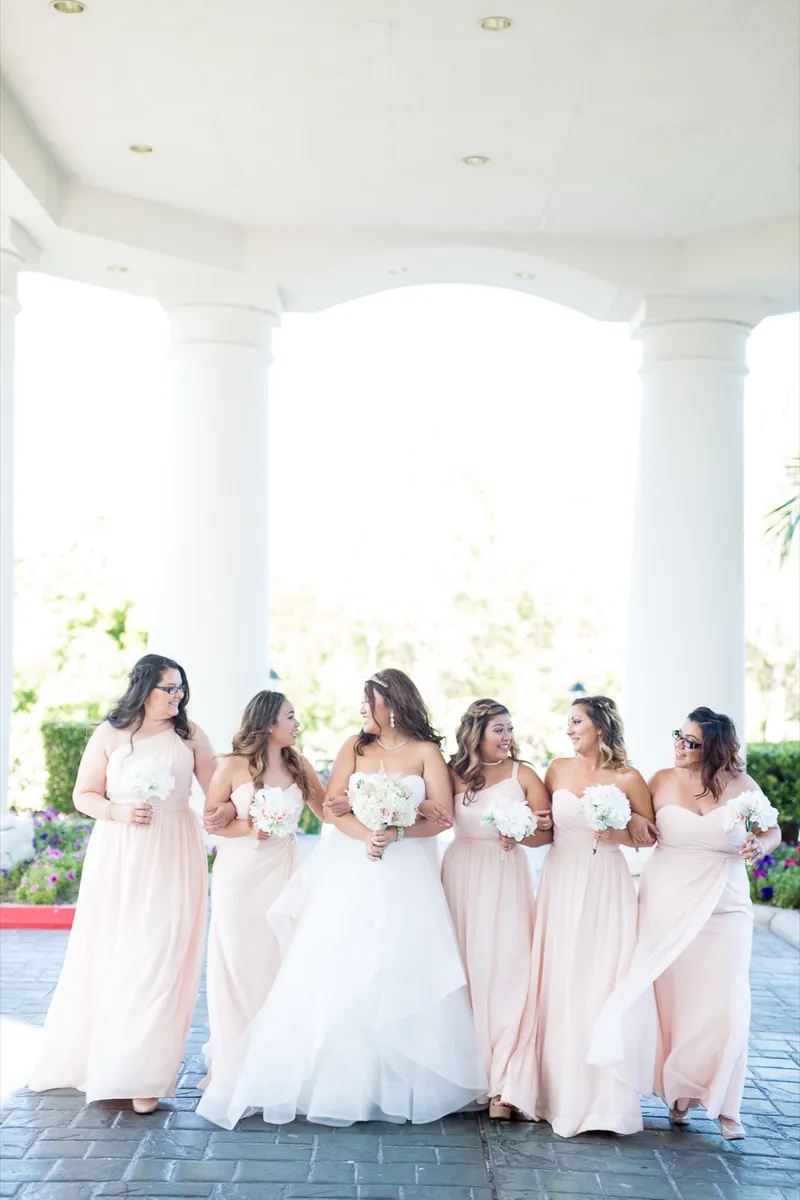 Bride and her bridesmaids walking together between the white columns of the portico