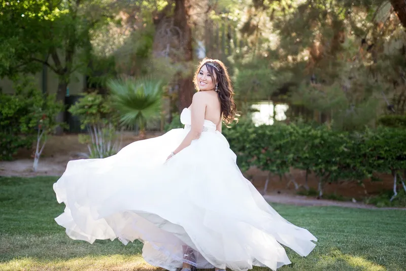 Bride swinging her tulle skirt out wide on the lawn with palms and shrubs behind her