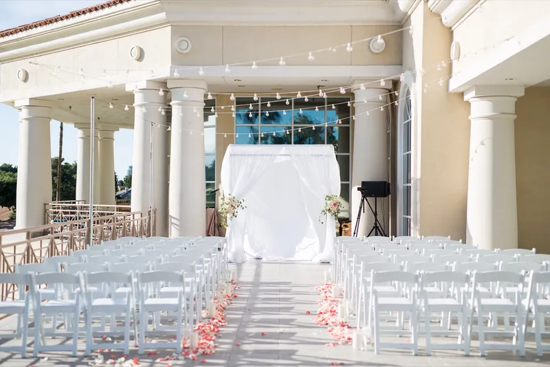 Empty ceremony set under the portico, white chairs on both sides of a petal lined aisle with cafe lights strung overhead