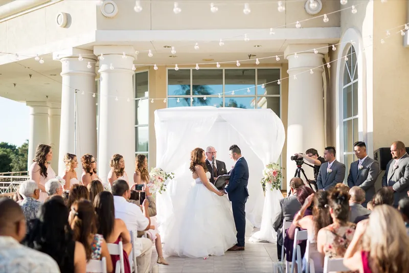 Ceremony under the clubhouse portico, the couple facing the officiant with the wedding party and seated guests around them