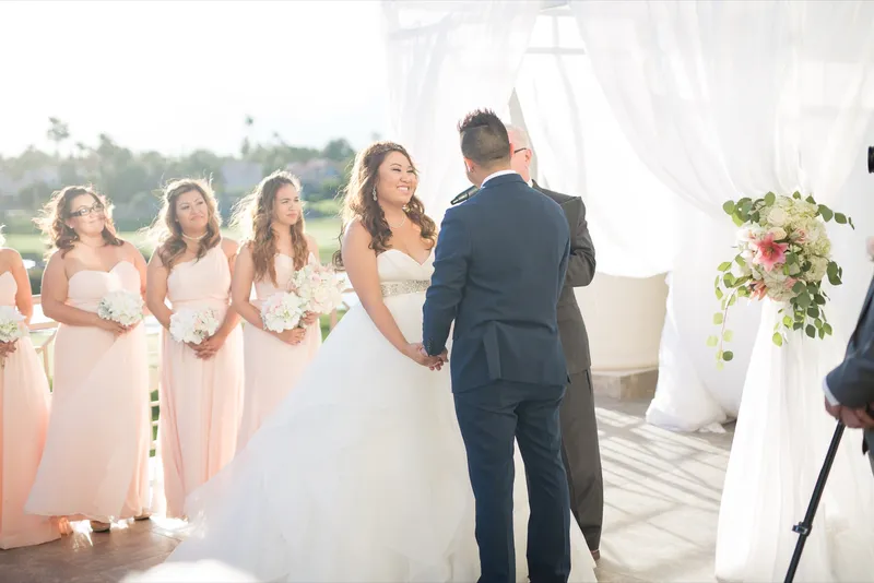 Bride and groom facing each other at the altar with the officiant behind them and bridesmaids in blush to one side