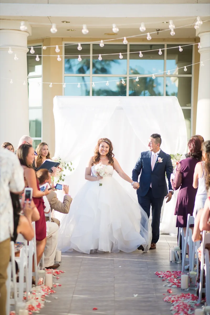 Newlyweds walking back down the petal strewn aisle as guests raise their phones
