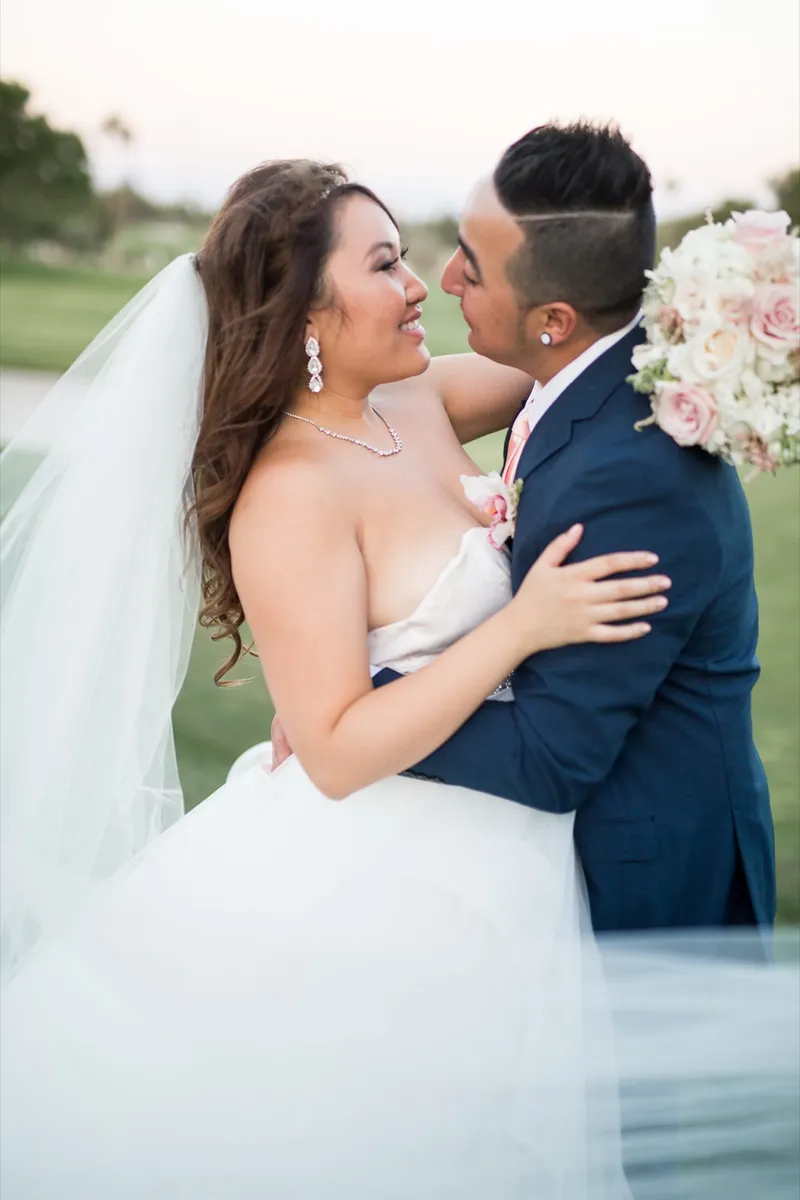 Bride and groom cheek to cheek with her veil lifted around them and the bouquet raised beside their faces