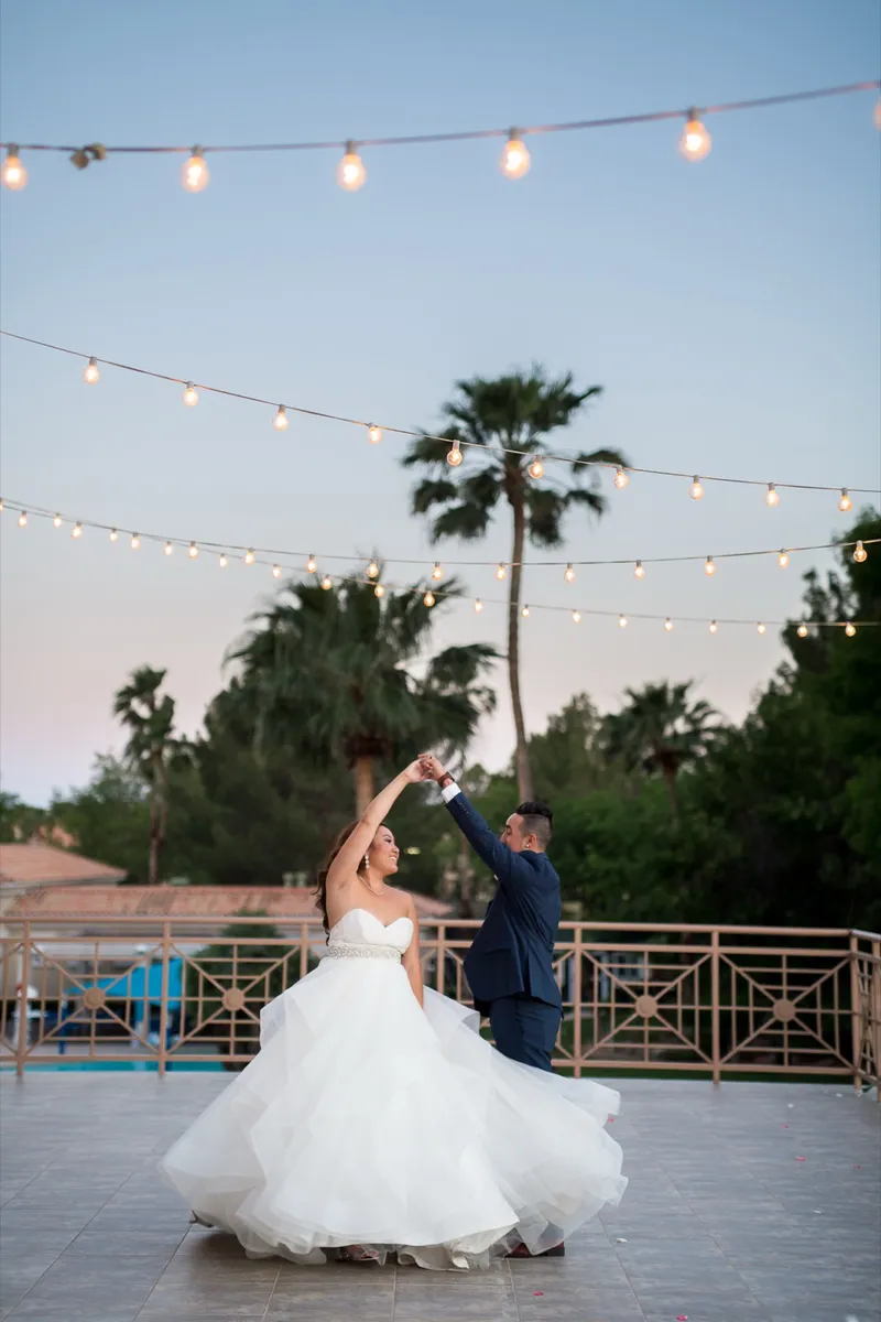 Couple dancing on the outdoor terrace at dusk under strung lights with palms behind them