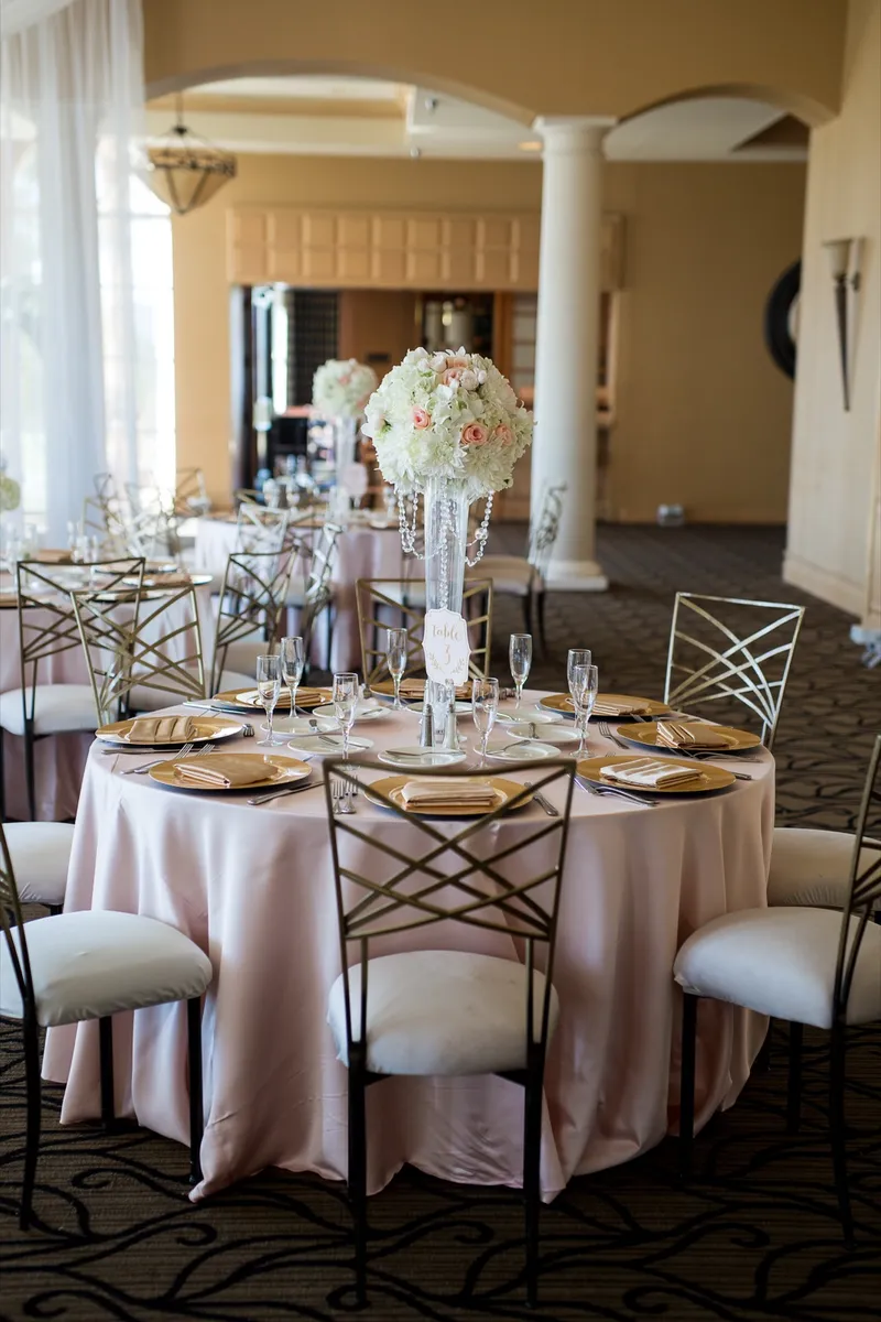 One round table set with gold chargers and folded gold napkins beneath a tall crystal centerpiece