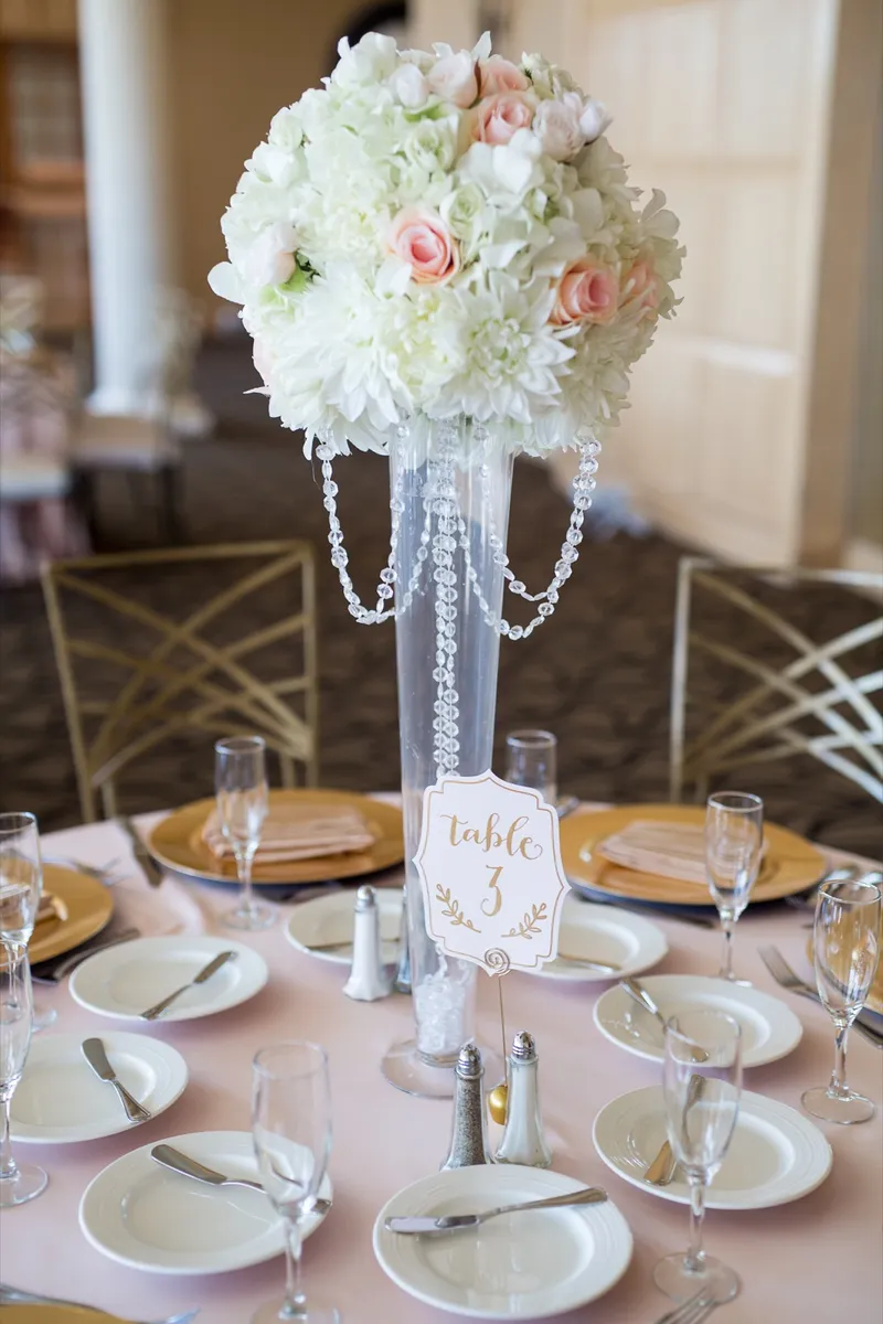 Tall crystal centerpiece of white and blush roses above the table three card and the gold place settings