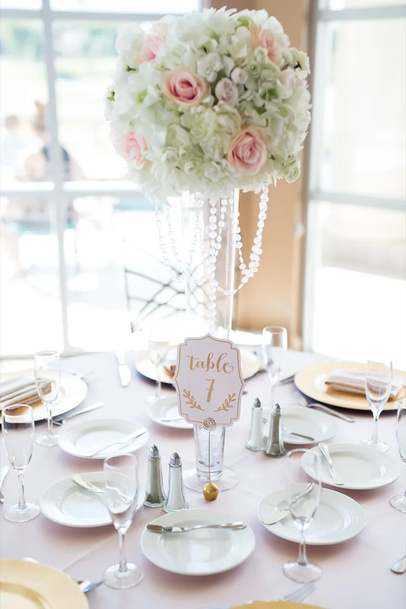 Blush and white centerpiece on a crystal stand at table one beside the ballroom windows