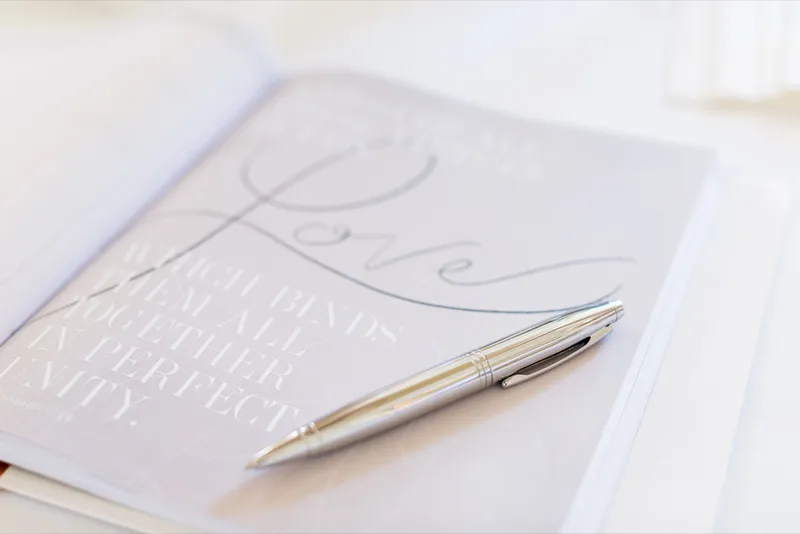 Calligraphy guest book lying open on a white surface with a gold pen resting across the page
