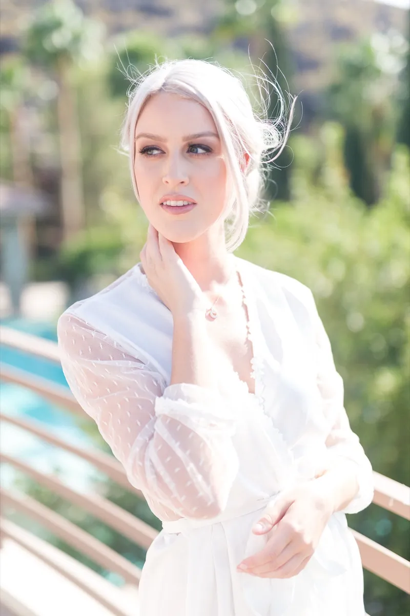 Bride in her robe standing outside by the pool in bright sun, hair pinned up, before getting dressed