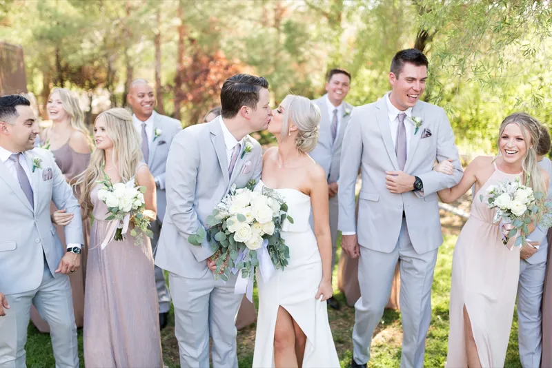 Bride and groom kissing in the middle of the whole wedding party as everyone walks across the lawn together