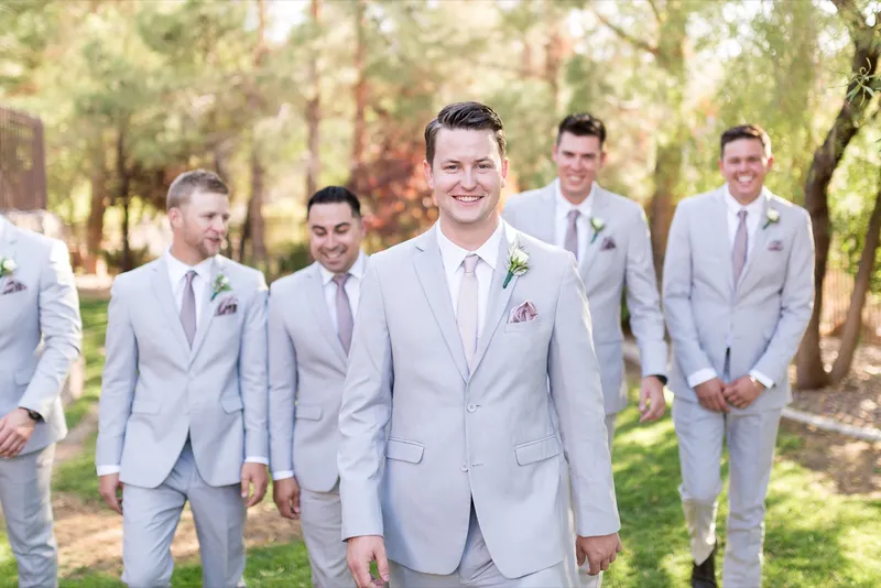Groom walking across the lawn with his groomsmen, all in light grey suits with blush ties