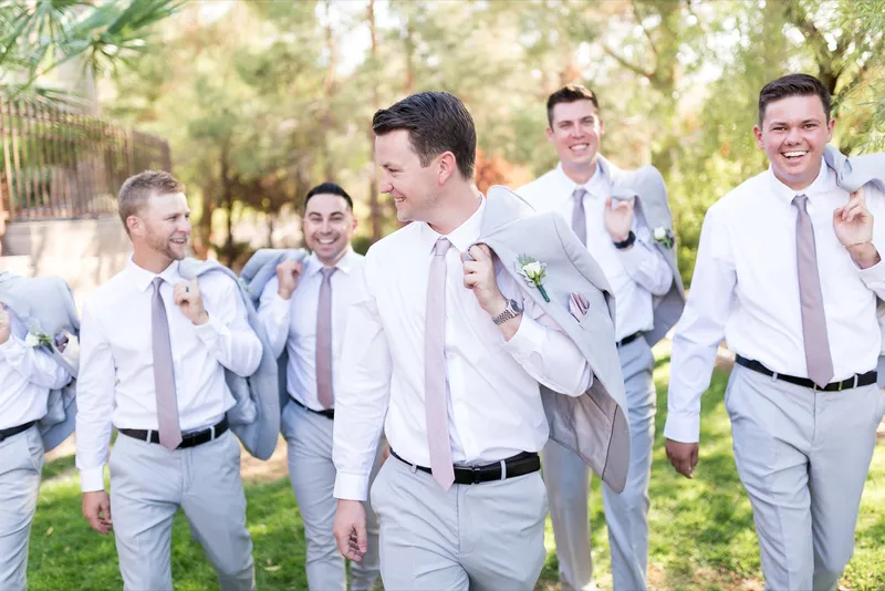 Groomsmen walking together with their suit jackets slung over their shoulders, talking and laughing