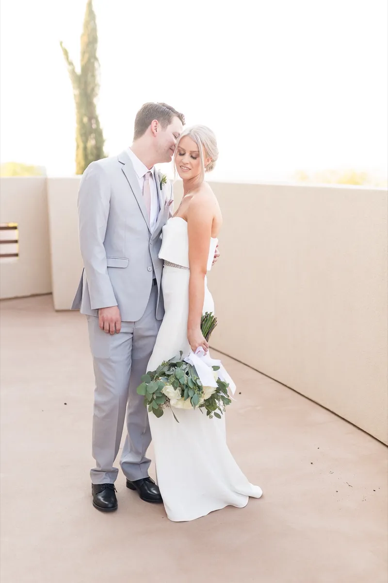 Groom kissing the top of the bride's head on the terrace, the valley falling away behind them