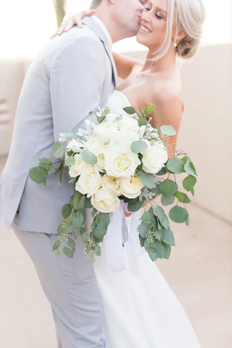 Couple kissing with the bride's white rose bouquet held out to the side of the frame