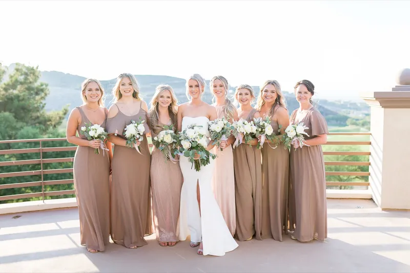 Bride and her bridesmaids in taupe gowns standing along the curved terrace with the hills behind them