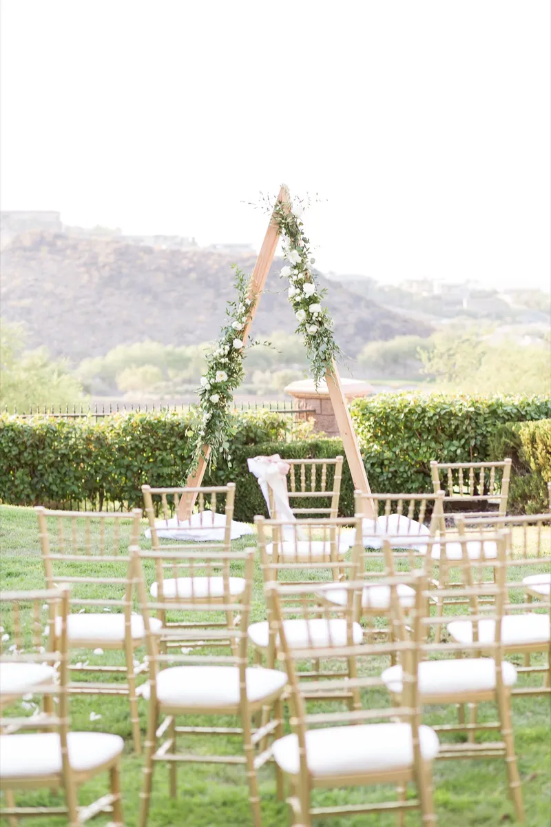 Closer view of the greenery covered triangle arch with fabric pooled at its feet and gold chairs in the foreground