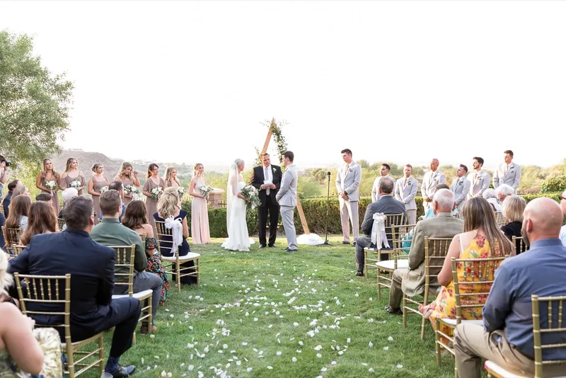 The ceremony seen from the back of the lawn over the heads of the seated guests, the couple small at the arch
