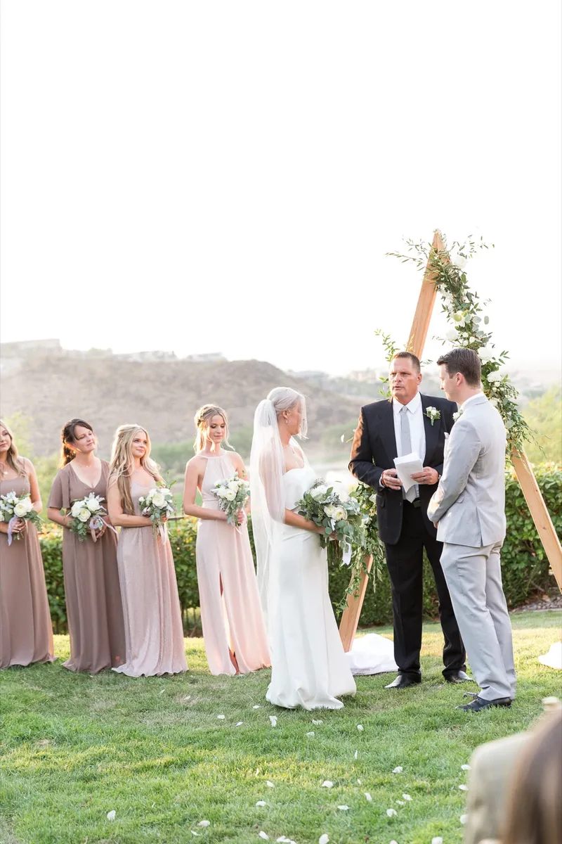 Couple standing at the arch with the bridesmaids in mauve on one side and the officiant beside them