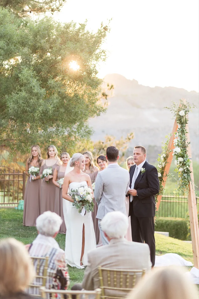The ceremony in low golden light, the wedding party watching from both sides of the arch