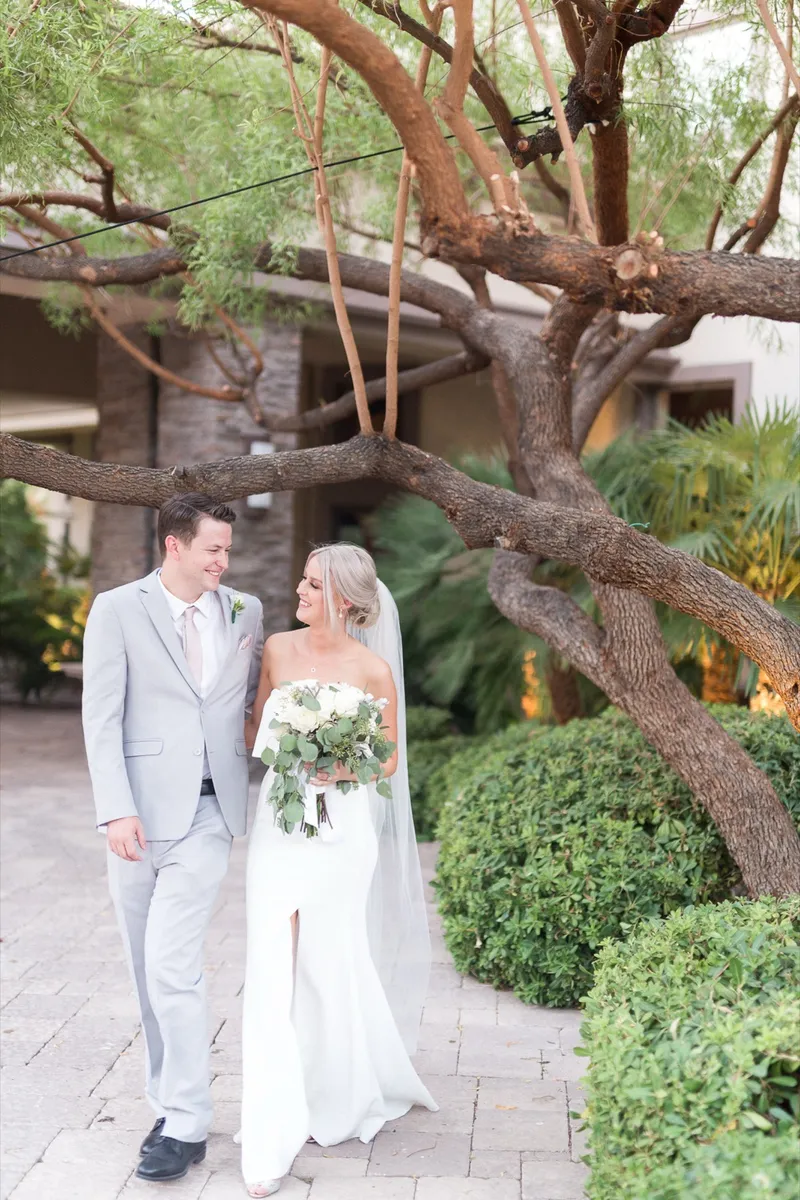 Couple standing together on the pavers under a big sprawling tree beside the house