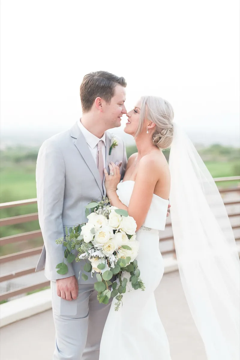 Couple touching noses at the terrace rail with the veil catching the breeze around them